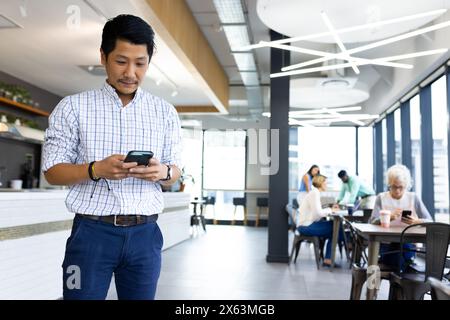 Diverse team working at office while Asian male checking smartphone in cafe Stock Photo