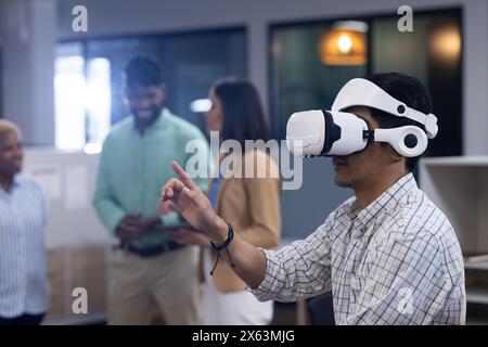 At office, Asian man wearing VR headset pointing, surrounded by a team, copy space Stock Photo