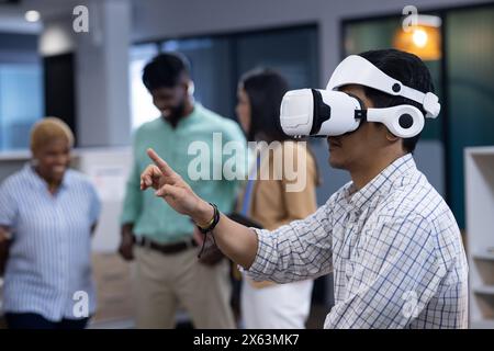 A diverse team in office, Asian man using VR headset, pointing at something Stock Photo