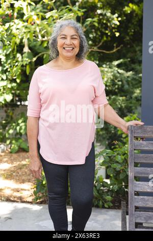 Senior biracial woman enjoying outdoors, leaning on bench, smiling Stock Photo