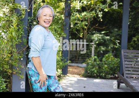 Outdoors, Asian senior female wearing blue top and patterned leggings, smiling, copy space Stock Photo