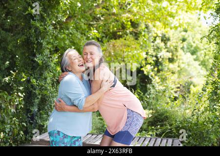 Outdoors, diverse senior female friends, Asian and Caucasian, hugging Stock Photo