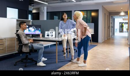 In modern office, diverse young team working and chatting Stock Photo