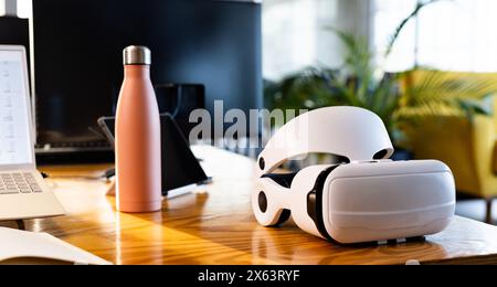 At office, VR headset resting on a wooden desk next to a laptop Stock Photo
