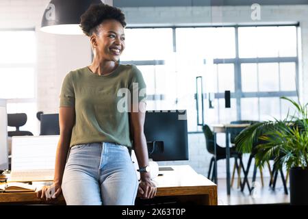 At office, African American businesswoman leaning on desk, looking away Stock Photo