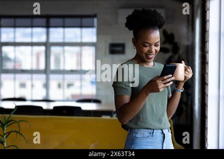 At office, African American businesswoman checking smartphone, wearing casual Stock Photo