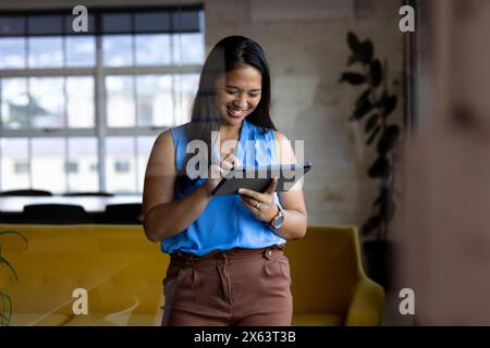 At office, biracial businesswoman using tablet, standing Stock Photo