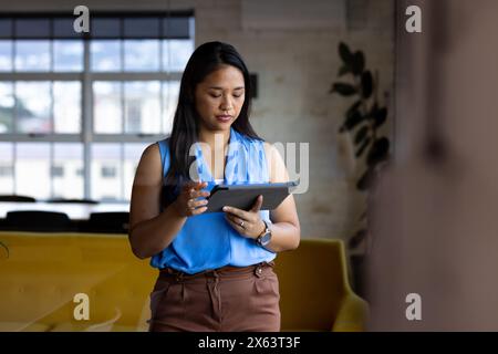 At office, biracial businesswoman holding tablet, looking focused Stock Photo