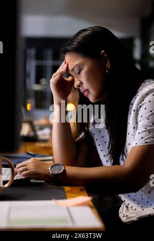 At office, working late, biracial businesswoman focusing on spreadsheet Stock Photo