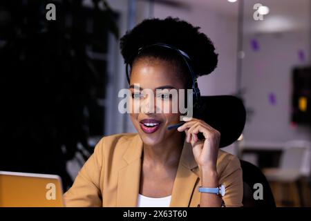 African American businesswoman in headset speaks to laptop, working late Stock Photo