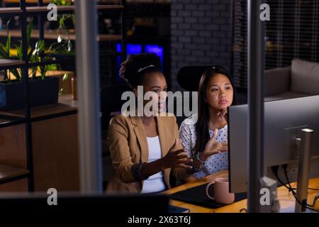 At office, diverse female business colleagues discussing over computer, working late Stock Photo