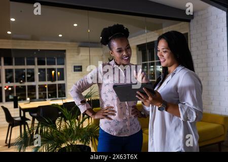 At office, diverse female colleagues discussing tablet, working late Stock Photo