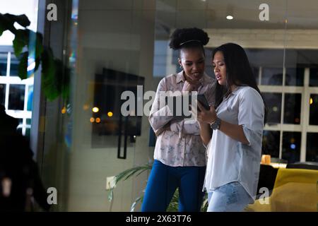 At office, diverse female business colleagues studying tablet, working late Stock Photo