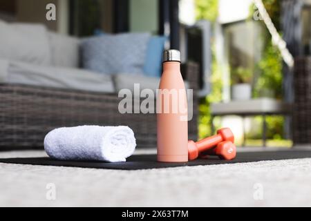 At home, rolled-up white towel, pink water bottle, and dumbbells resting on mat Stock Photo