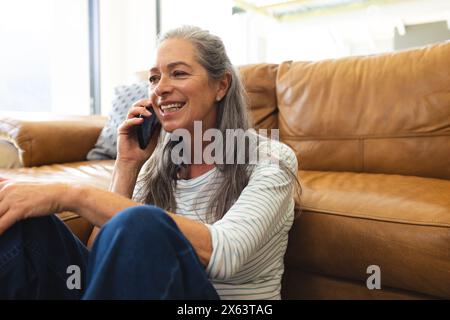 At home, mature Caucasian woman talking on a smartphone, sitting on a couch Stock Photo