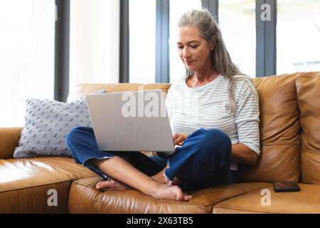 At home, mature Caucasian woman sitting on a sofa, using a laptop Stock Photo