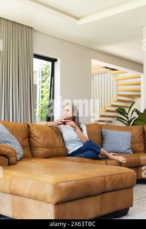 At home, mature Caucasian woman holding smartphone, sitting on sofa Stock Photo