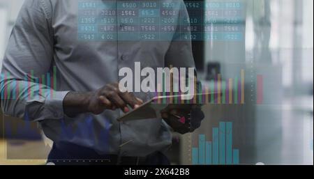Image of graphs and number charts, senior african american man scrolling on digital tablet Stock Photo