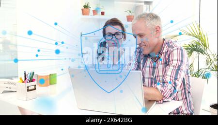 Image of security padlock icon against diverse man and woman discussing over a laptop at office Stock Photo