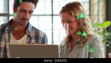 Image of two globes of digital icons against caucasian man and woman over a laptop at office Stock Photo