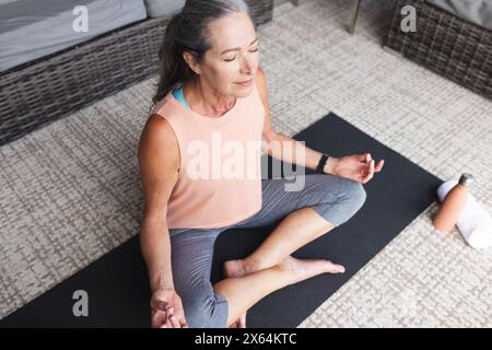 At home, mature caucasian woman wearing pink, meditating on yoga mat Stock Photo