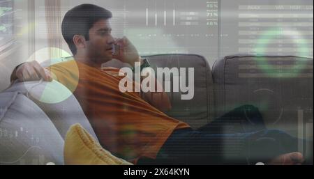 Image of infographic interface over biracial man sitting on sofa and talking on smartphone Stock Photo