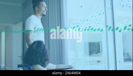 Image of graphs over diverse man and woman on wheelchair looking through glass window Stock Photo