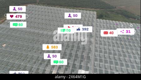 Image of social media icons floating against aerial view of solar panels in grassland Stock Photo