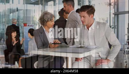 Image of multiple graphs, numbers over caucasian coworkers discussing reports on digital tablet Stock Photo