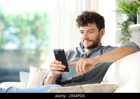Serious man using smart phone sitting on a couch at home Stock Photo