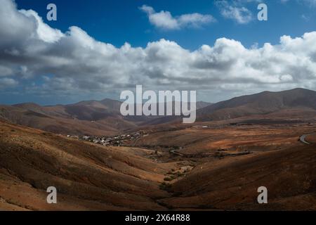 A mountain range with a cloudy sky in the background. The sky is mostly blue with some clouds scattered throughout. The mountains are covered in trees Stock Photo