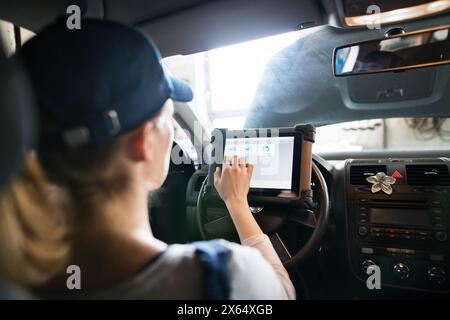 Female auto mechanic using diagnostic tool, scanner, running diagnostic on car. Beautiful woman sitting inside of car, performing diagnostic test. Stock Photo