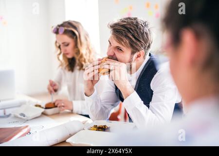 Young group of colleagues having quick lunch togeter in a startup company office. Working in co-working space. Stock Photo