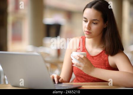 Serious woman is using laptop and drinking coffee in a restaurant terrace Stock Photo