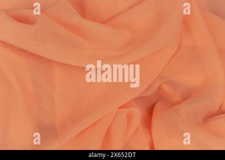 Peach fuzz colour background. Apricot colour pattern. Chiffon fabric. Fold satin background. Silk fabric background. Orange textile. Elegant decor. Stock Photo