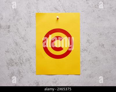 Patenting and copyright protection. Copyright symbol on a yellow sheet of paper pinned to a white concrete wall. Stock Photo