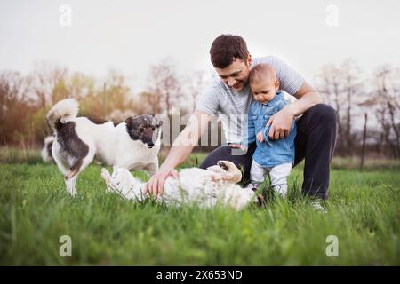 Father and little toddler boy playing with dogs, having fun during warm spring day. Father's day concept. Family time outdoors. Stock Photo