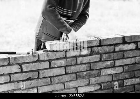 a man builds a brick wall, puts a brick on a cement-sand mortar, removing excess mortar with a trowel black white photo Stock Photo