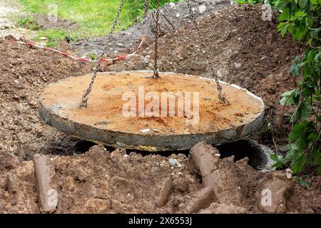 reinforced concrete well cover made of concrete rings hanging on iron chains with hooks Stock Photo