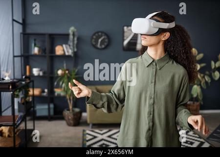 Medium shot of modern biracial girl standing in living room at home using VR headset, copy space Stock Photo