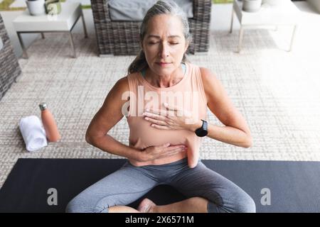 At home, mature Caucasian woman sitting cross-legged, practicing yoga Stock Photo