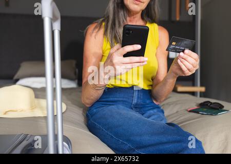 At home, mature Caucasian woman holding smartphone and credit card Stock Photo