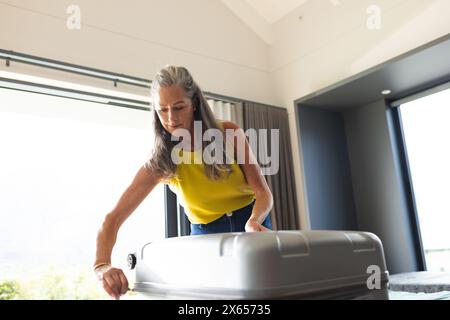 At home, Caucasian mature woman closing suitcase Stock Photo