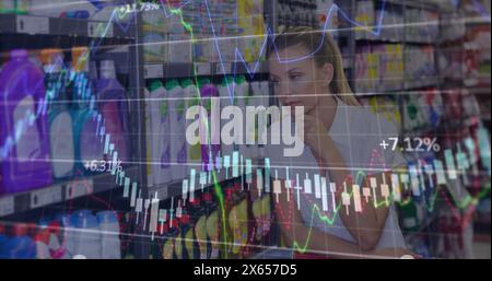 Image of financial data processing over thoughtful caucasian woman at grocery store Stock Photo