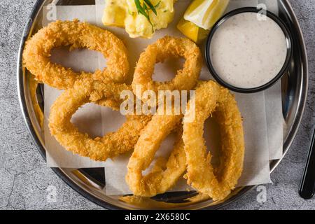 Fried calamari with potato salad next to it on stone table Stock Photo
