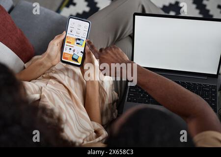 High angle view of unrecognizable biracial couple doing online shopping using app on smartphone and laptop with blank screen Stock Photo