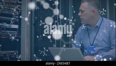 Image of molecules over stressed caucasian man working on laptop in server room Stock Photo