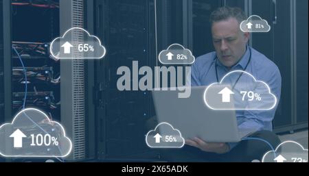 Image of clouds with numbers over stressed caucasian man working on laptop in server room Stock Photo
