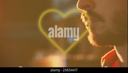 Image of yellow heart neon text over caucasian man drinking beer in bar Stock Photo