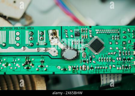 Detailed close-up shot of damaged electronic circuit board highlighting burnt components and intricate microchips on vibrant green background. Stock Photo